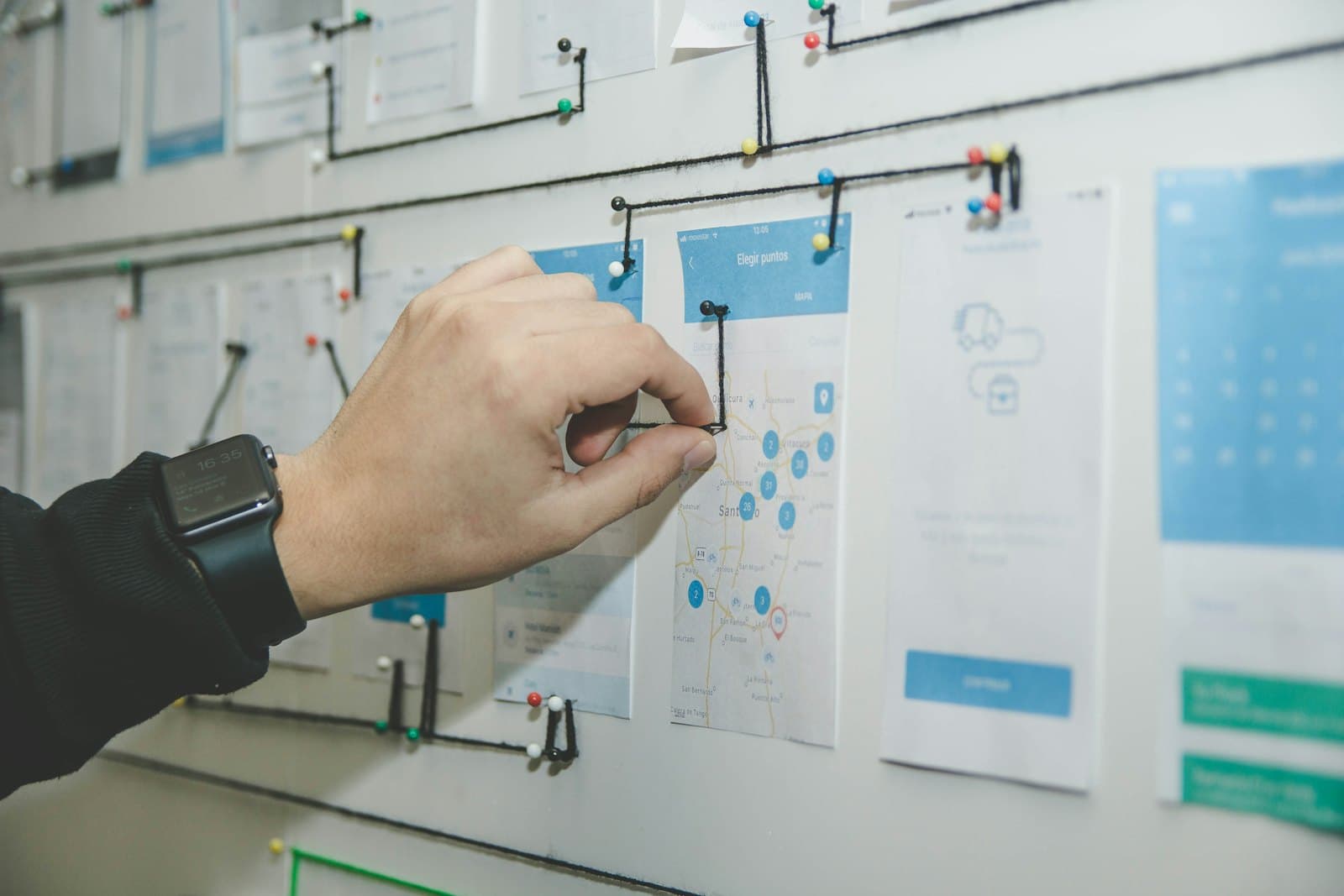 A hand connecting a journey map pinned across printed product screens.